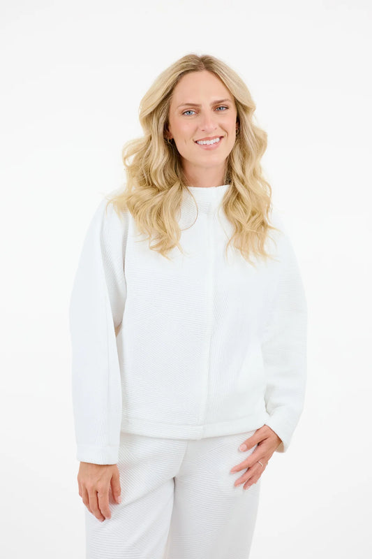 With long blonde hair and clad in a Shannon Passero Serafina Top, a person smiles brightly at the camera against a plain white background, defying the notion that life lacks color.