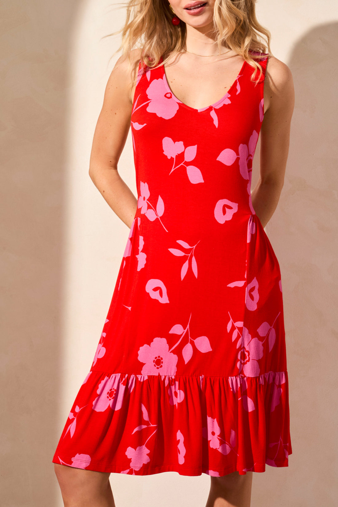 A woman poses against a light wall, highlighting a stylish Tribal Printed Sleeveless Dress featuring blue with white floral patterns, expertly paired with white wedge sandals.