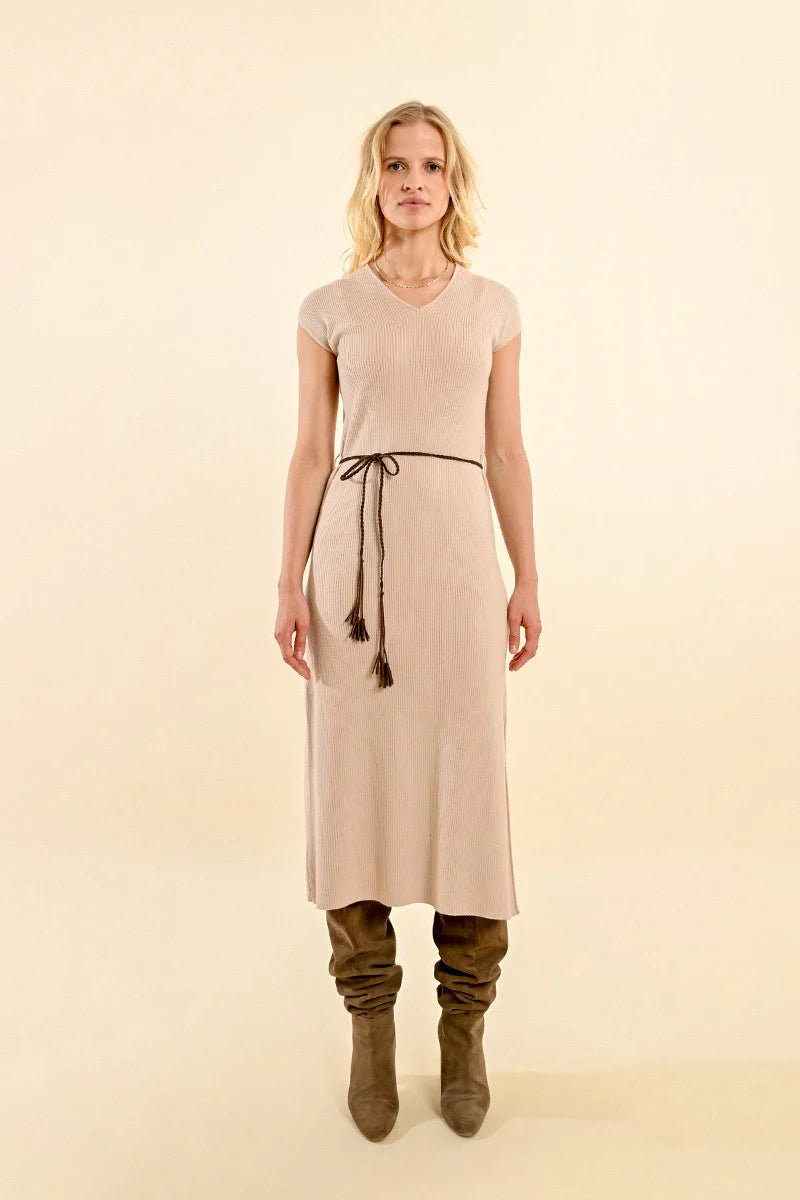 A person wearing the Molly Bracken Short Sleeve Ribbed Dress with Side Slit in beige, paired with a braided black belt and knee-high brown boots, stands against a light background.