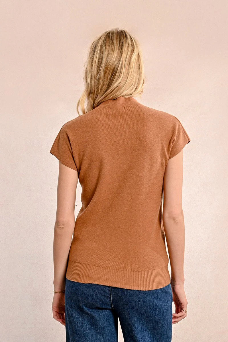 A person with long blonde hair is standing with their back to the camera, wearing a Short Sleeve Ribbed Sweater from Molly Bracken and blue jeans against a neutral background.