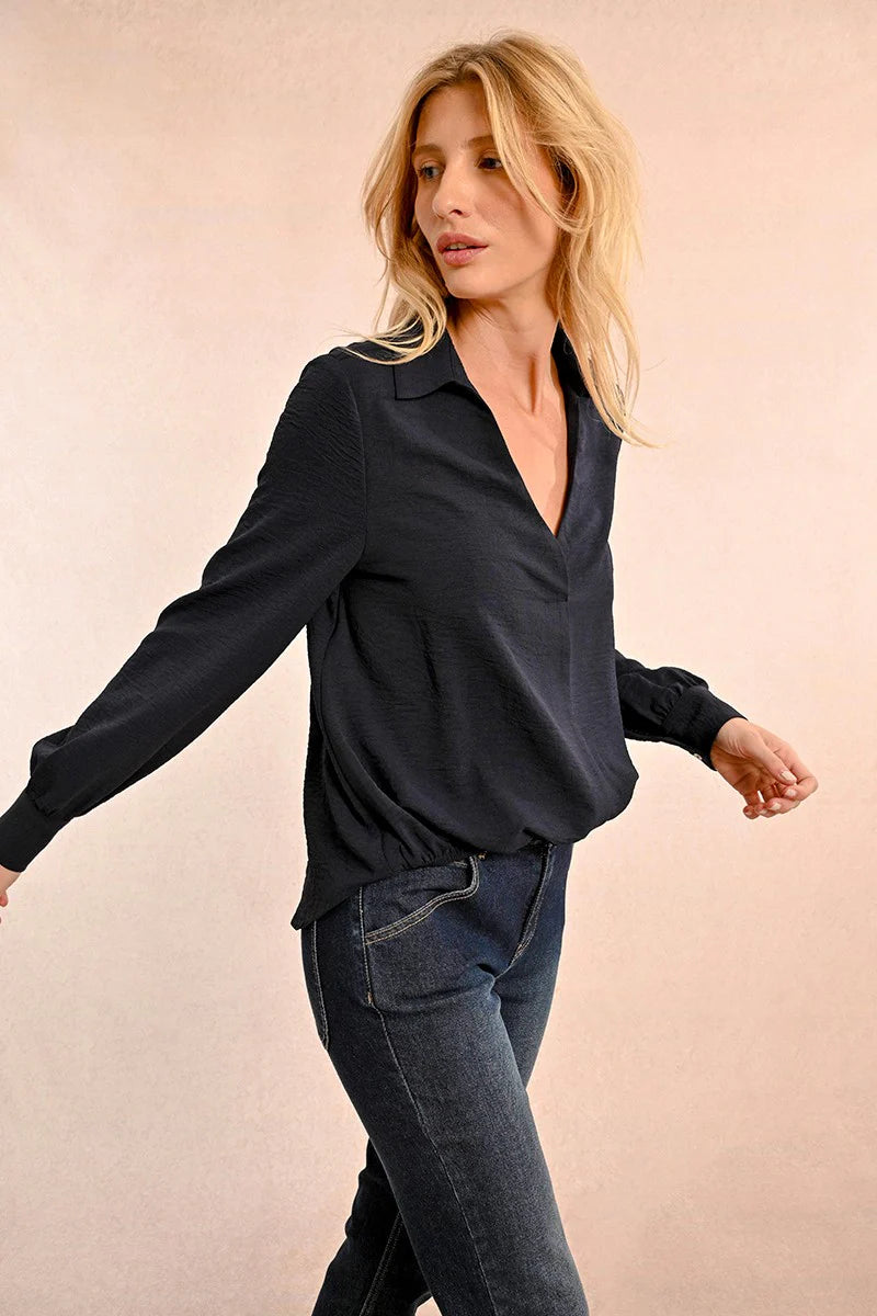 A woman with long blonde hair models a fashionable Short V Neck Puffy Blouse by Molly Bracken, paired with jeans, as she stands against a plain background.