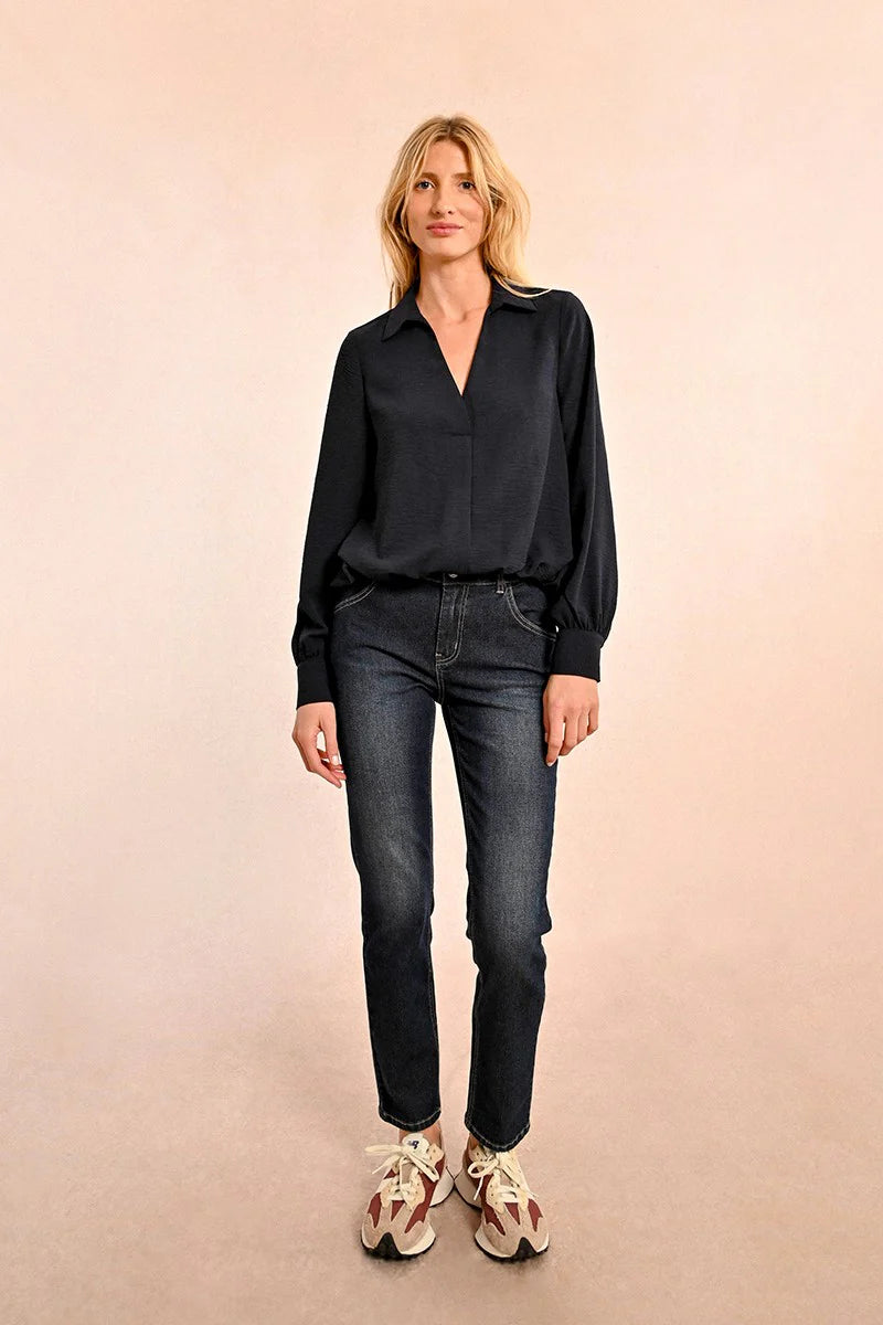 A woman with long blonde hair models a fashionable Short V Neck Puffy Blouse by Molly Bracken, paired with jeans, as she stands against a plain background.