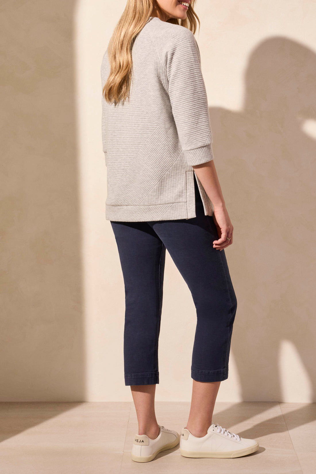 A person is wearing a light gray 3/4 Sleeve Tunic with Pockets by Tribal, paired with dark blue capri pants and white sneakers, standing against a neutral background.