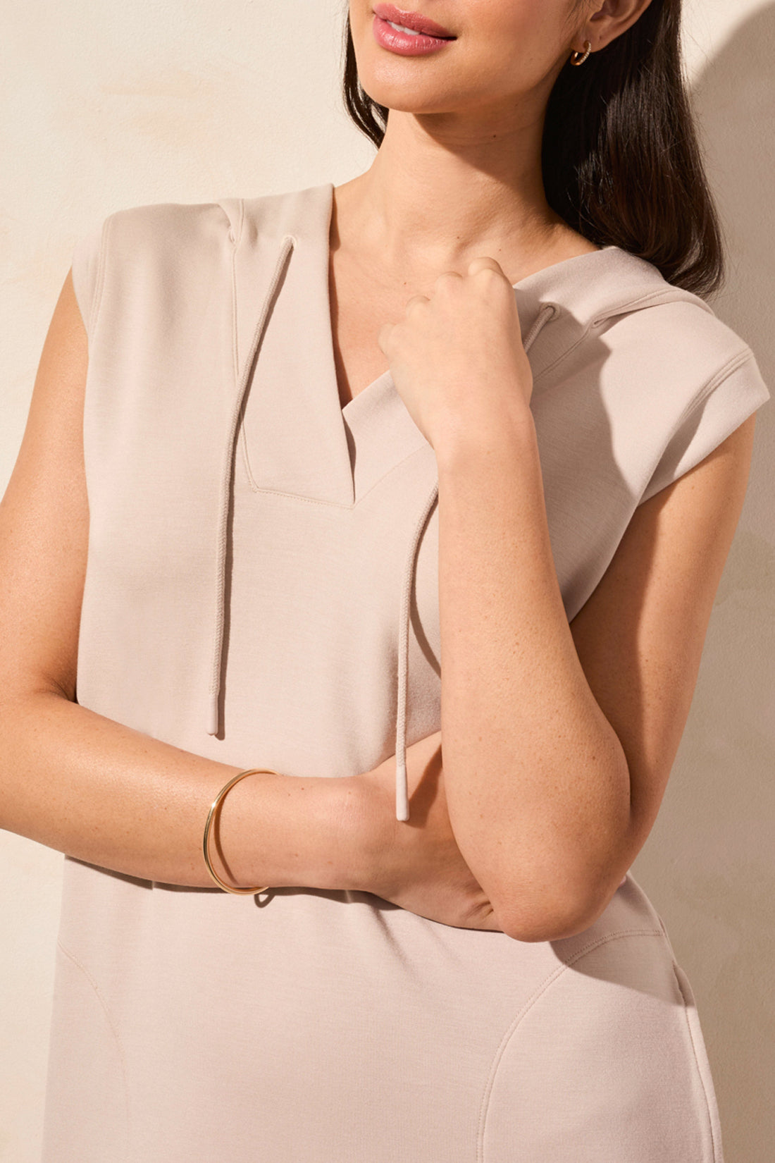 Someone stands against a beige wall, donning the Tribal sleeveless hooded dress with pockets in pink, paired with white sneakers.