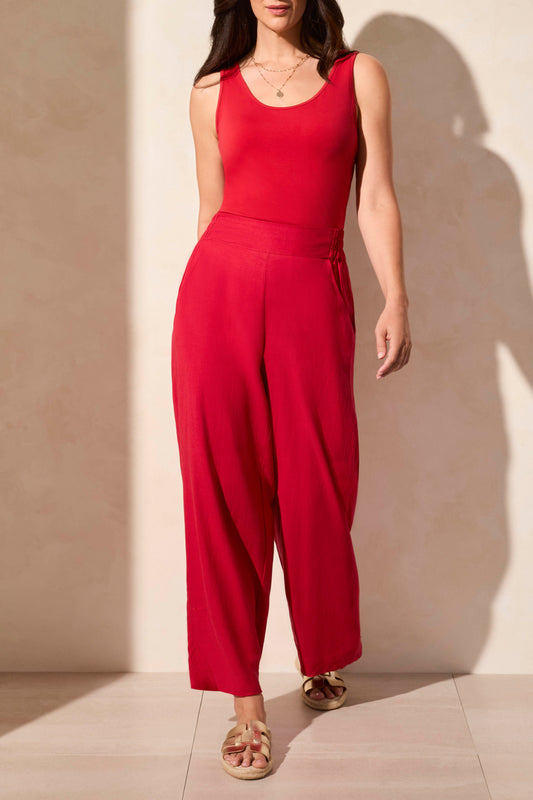 A woman in a sleeveless red top and Tribal's PULL ON ANKLE PANT W/ HEM VENT stands against a light background. Her look is super cute, completed by comfy open-toed sandals.