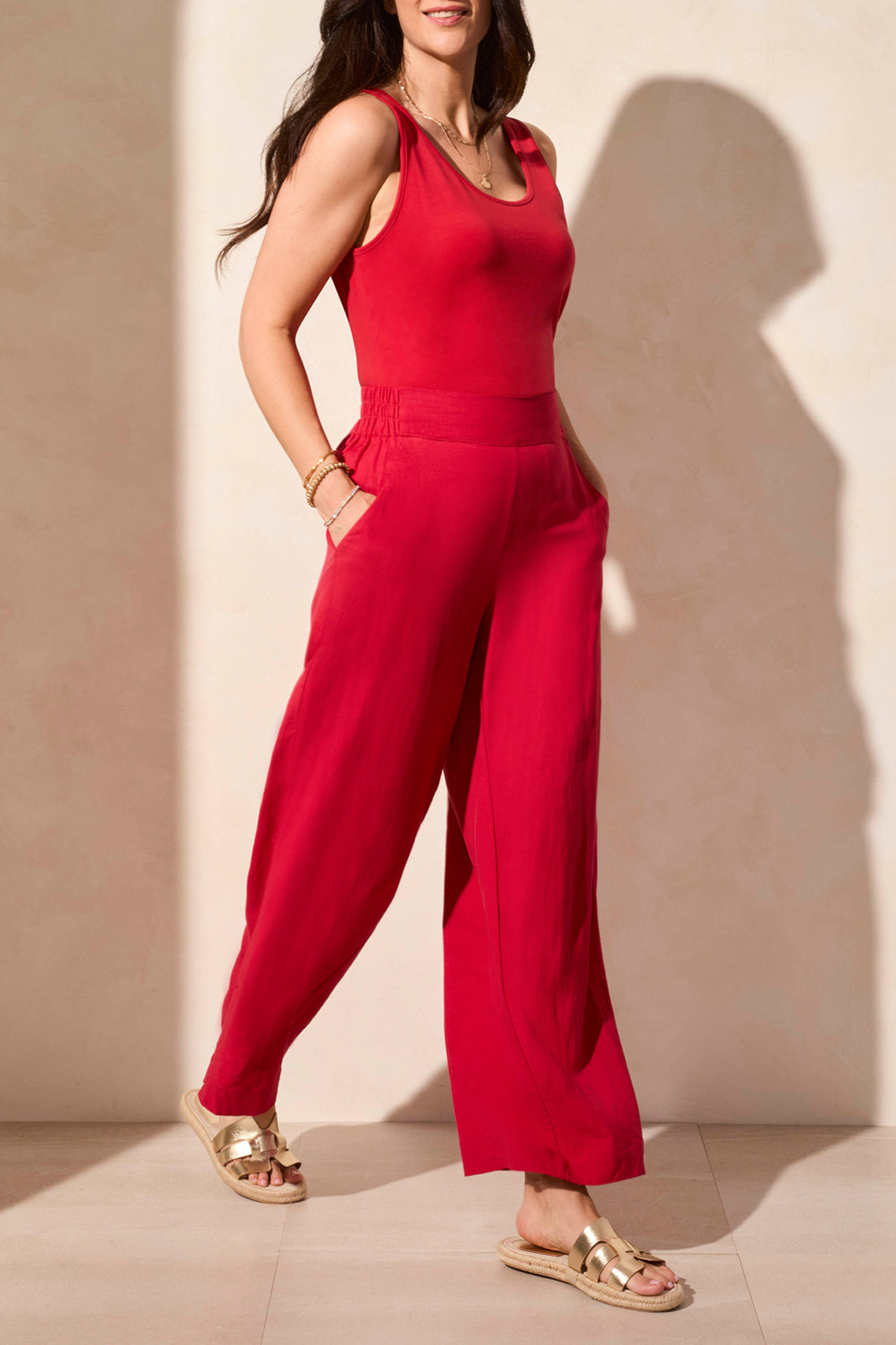 A woman in a sleeveless red top and Tribal's PULL ON ANKLE PANT W/ HEM VENT stands against a light background. Her look is super cute, completed by comfy open-toed sandals.