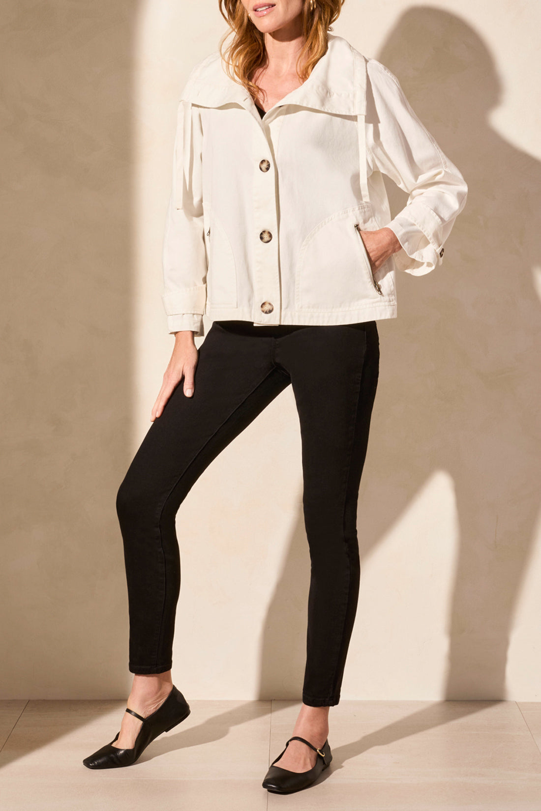 A woman models the Tribal's LONG SLEEVE BUTTON COAT in white, showcasing a cute style paired with a black top and pants against a plain backdrop.