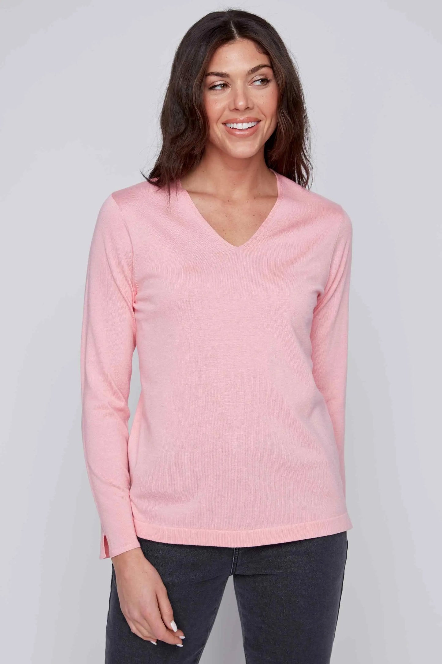 A person with long dark hair is wearing a stylish and cozy pink V Neck Pull Over by CoCo Y Club and dark pants, standing against a plain grey background.