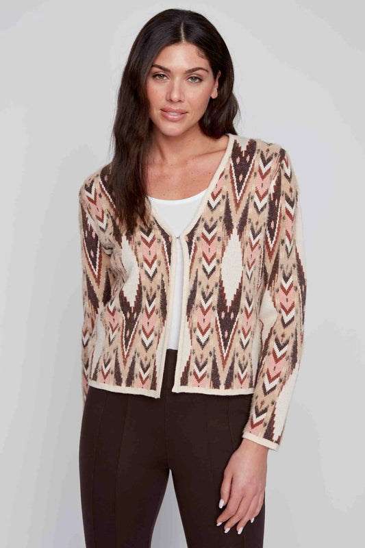 A woman with long dark hair dons a super soft Aztec Long Sleeve Cardigan by CoCo Y Club, showcasing its beige and brown design over a white top and dark pants, as she stands against a plain background.