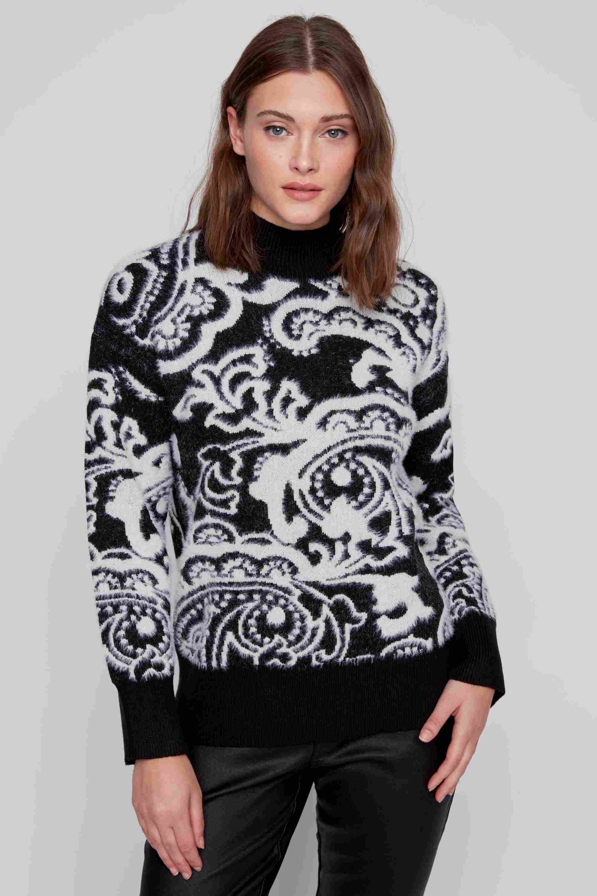 A person wearing a super soft CoCo Y Club High Neck Abstract Sweater with black cuffs and matching pants, striking a pose against a plain background. The sweater's black and white pattern brings a cute and cozy vibe to the overall look.