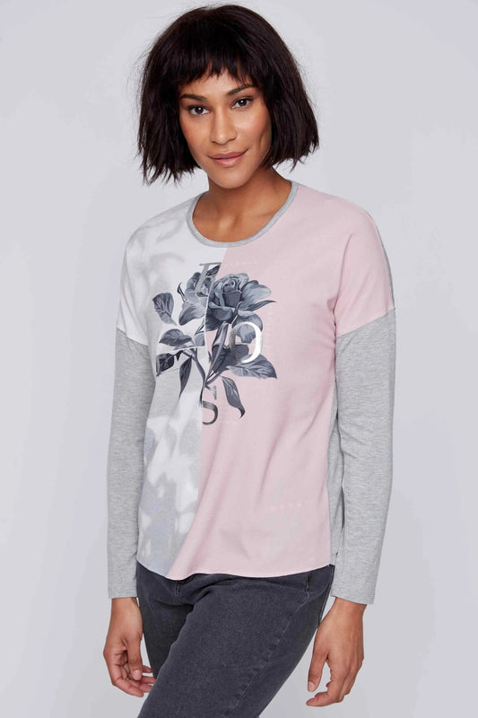 A person with short dark hair wears the CoCo Y Club Two Tone Long Sleeve Round Neck Top, showcasing a floral print, paired with dark pants, standing against a plain background.