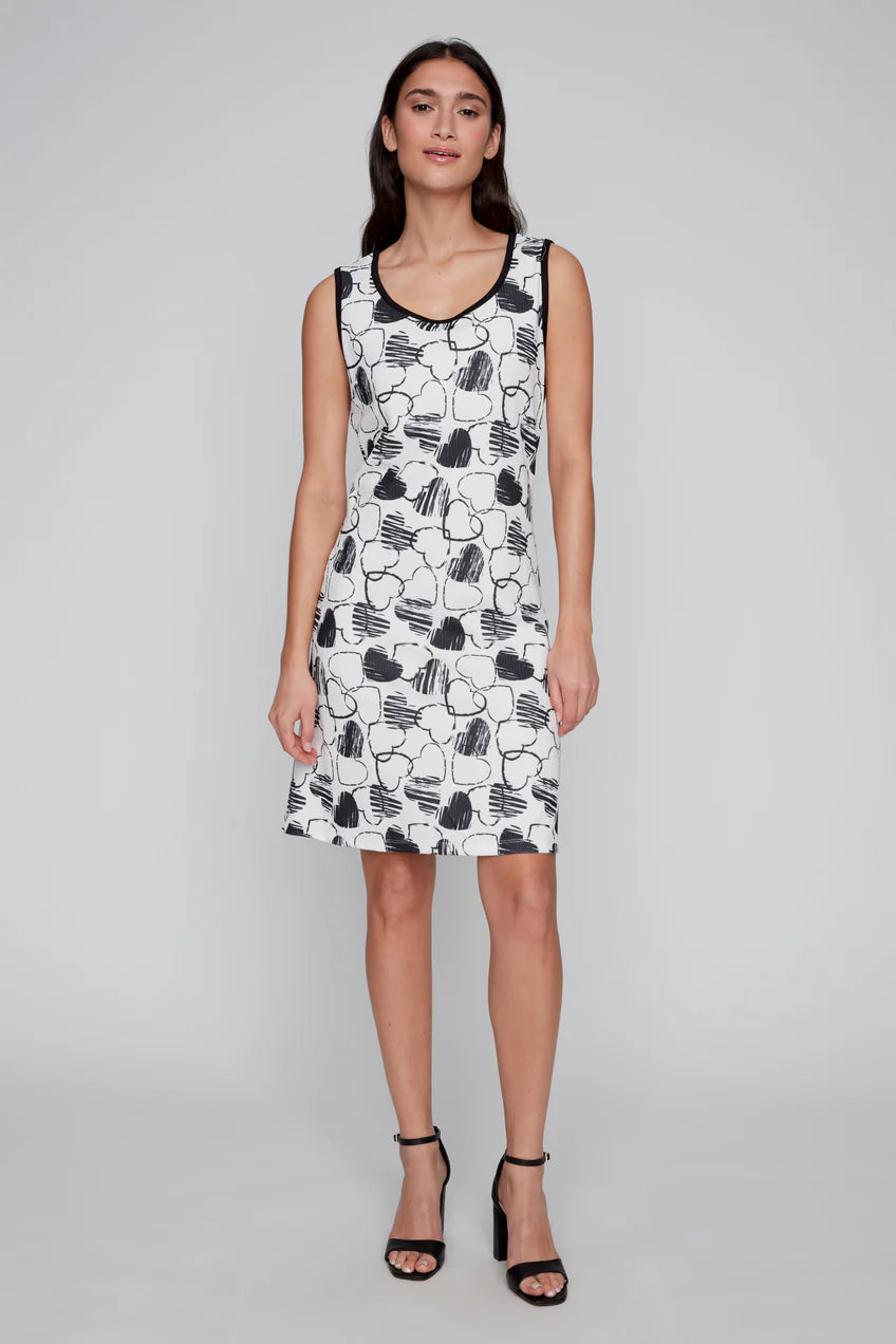 Against a gray background, the woman exudes confidence in her fashionable CoCo Y Club Black & White Heart Dress, characterized by its stylish two-tone design and sleeveless black and white floral pattern, paired elegantly with black heeled sandals.