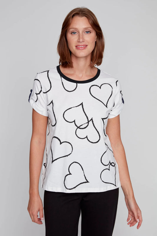 A person stands against a plain background, wearing a CoCo Y Club T-Shirt of Hearts featuring black-outlined hearts on white, paired with classic black pants.