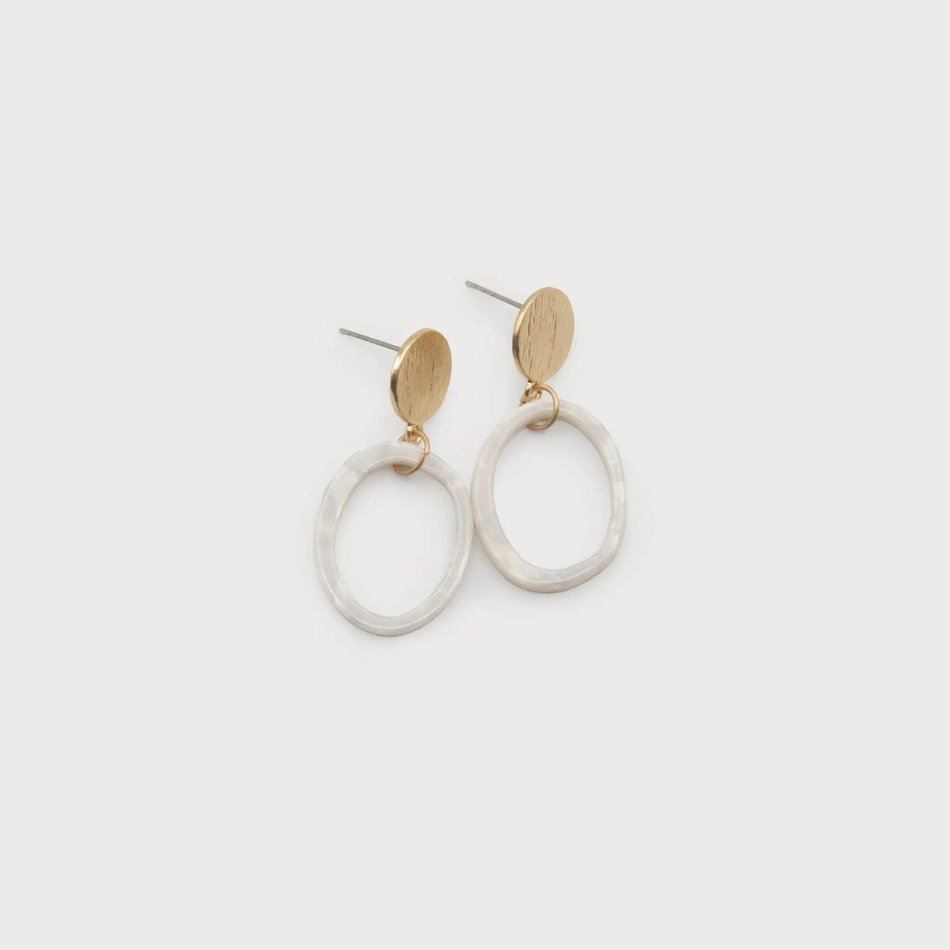 A pair of Resin Hoop Earrings from Caracol, showcasing round gold-colored studs with metal posts and open white resin rings.