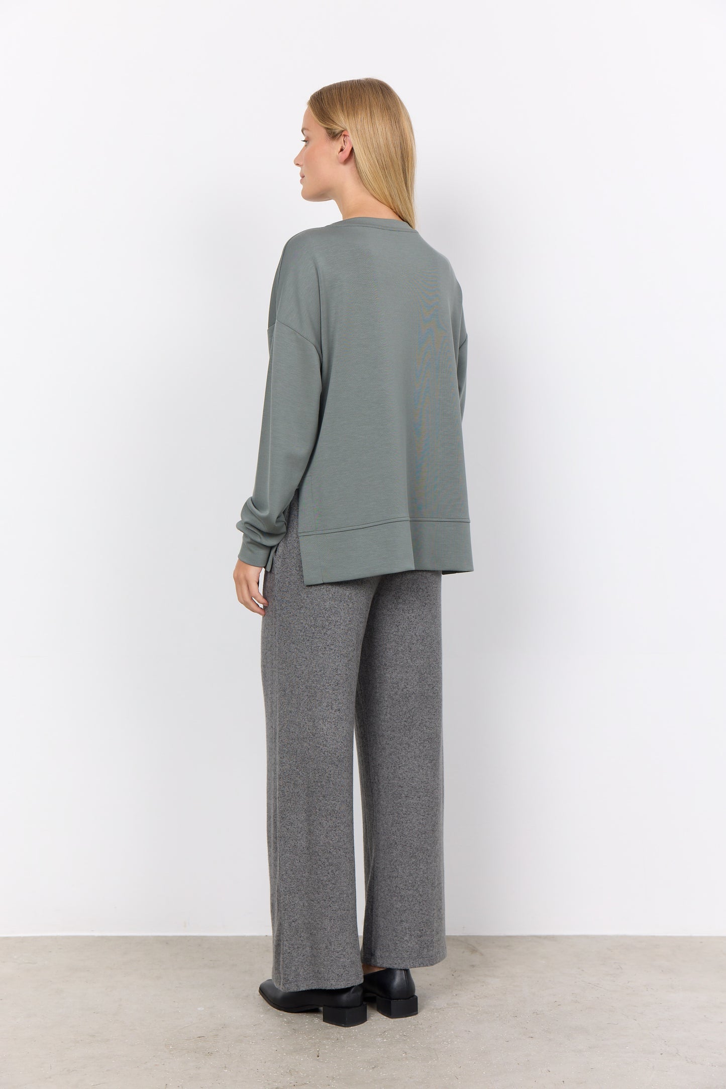 A person wearing a loose-fit Banu 164 Sweater by Soya Concepts in gray stands against a plain white background, paired with pants.