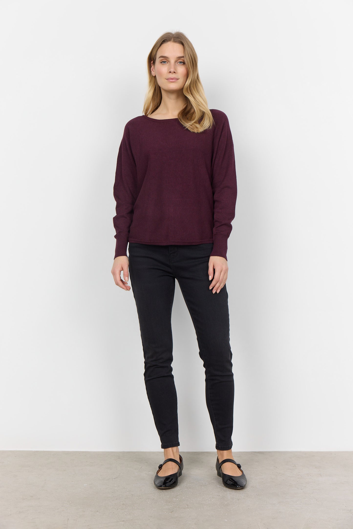 A person with long blond hair is wearing a comfortable Soya Concepts Dollie 620 Long Sleeve Sweater in maroon with button detail, paired with black pants, and is standing against a plain white background.