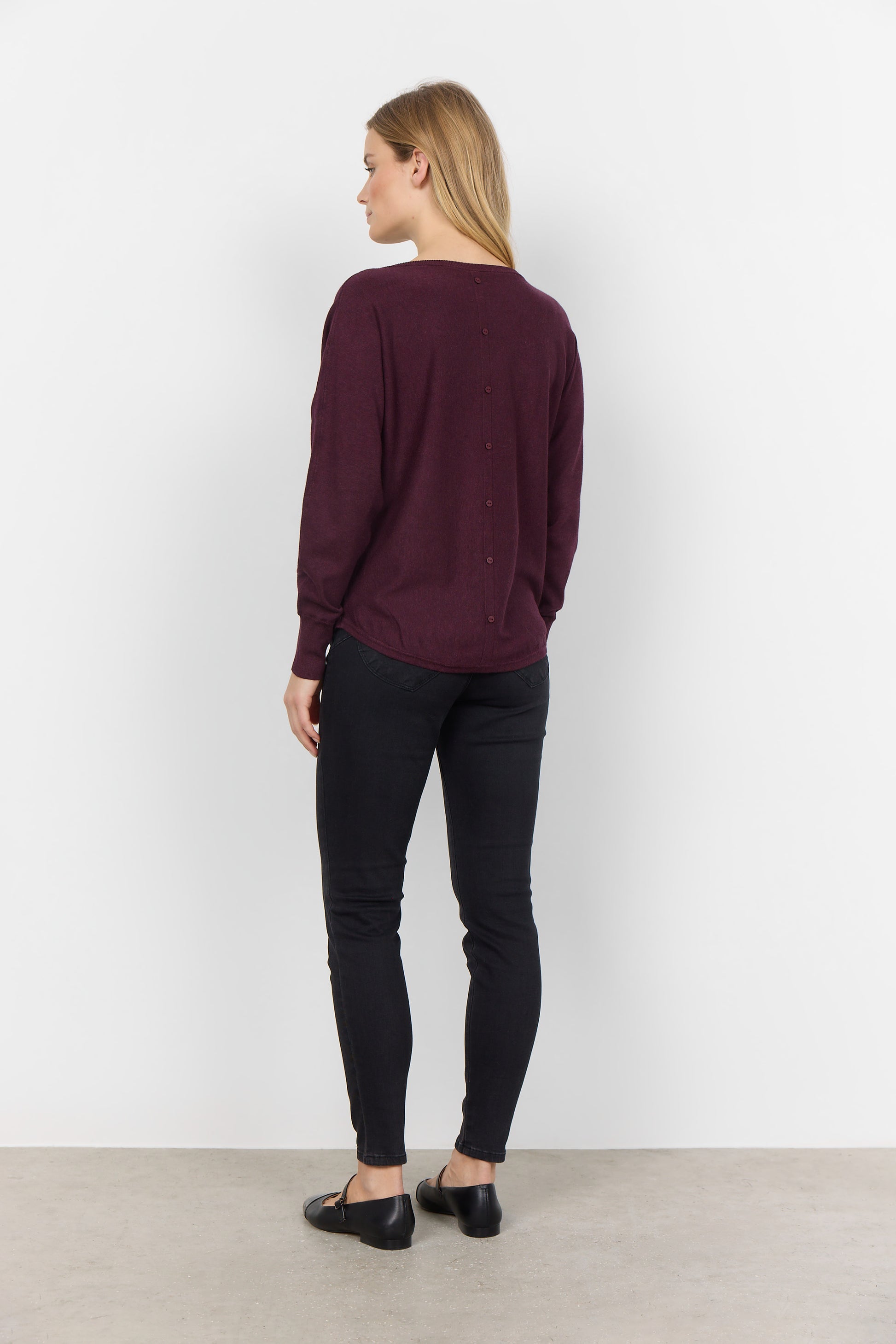 A person with long blond hair is wearing a comfortable Soya Concepts Dollie 620 Long Sleeve Sweater in maroon with button detail, paired with black pants, and is standing against a plain white background.