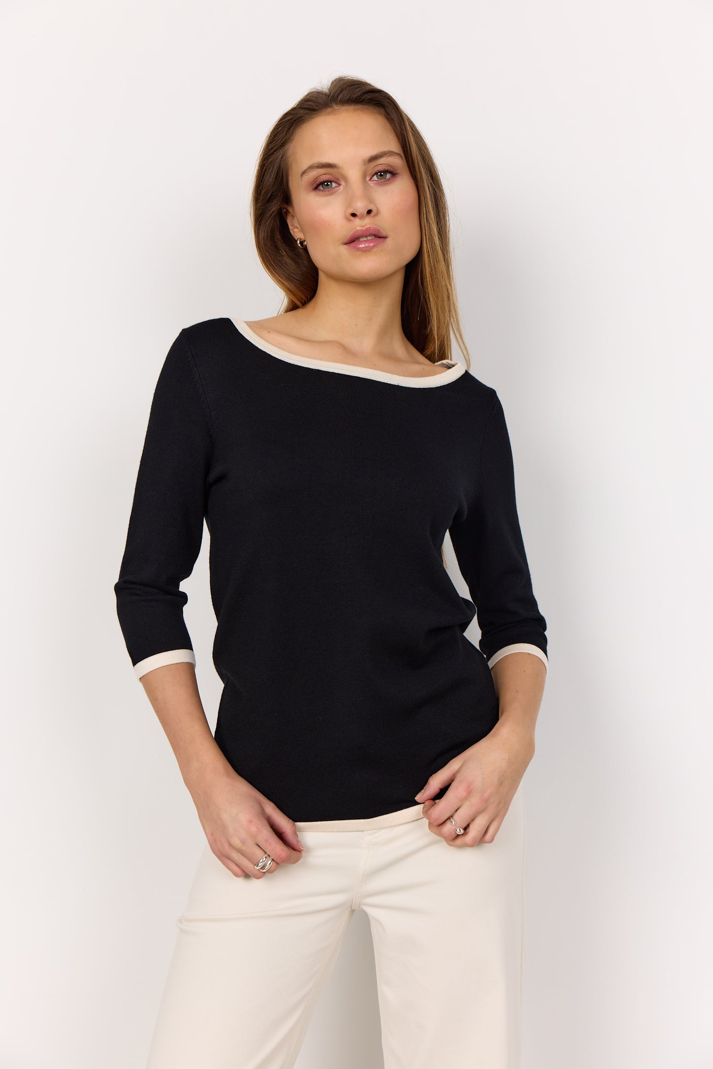 A person models the Soya Concepts Dollie 782 Sweater, featuring a sleek pullover design with a soft knit texture, paired with white pants against a plain white background.