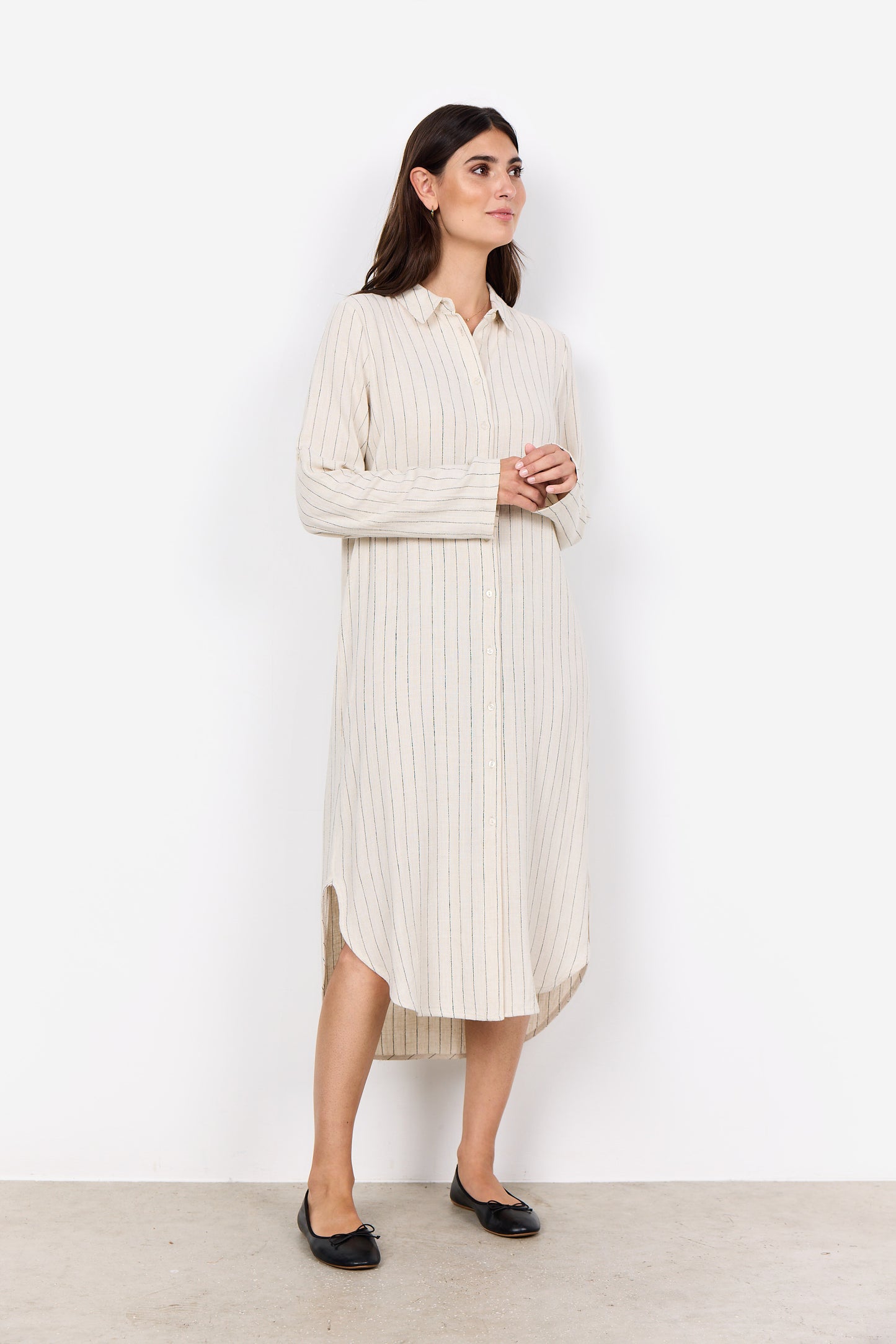 A woman stands against a plain white background, elegantly dressed in the Poula 4 Midi Dress by Soya Concepts, made from ECOVERO Viscose and featuring cream-colored vertical stripes with buttons down the front.