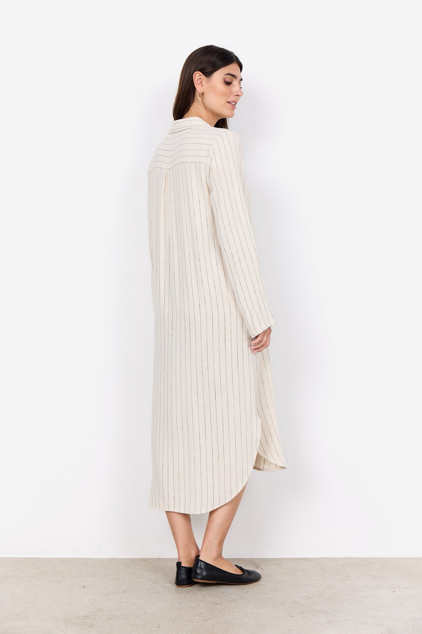 A woman stands against a plain white background, elegantly dressed in the Poula 4 Midi Dress by Soya Concepts, made from ECOVERO Viscose and featuring cream-colored vertical stripes with buttons down the front.