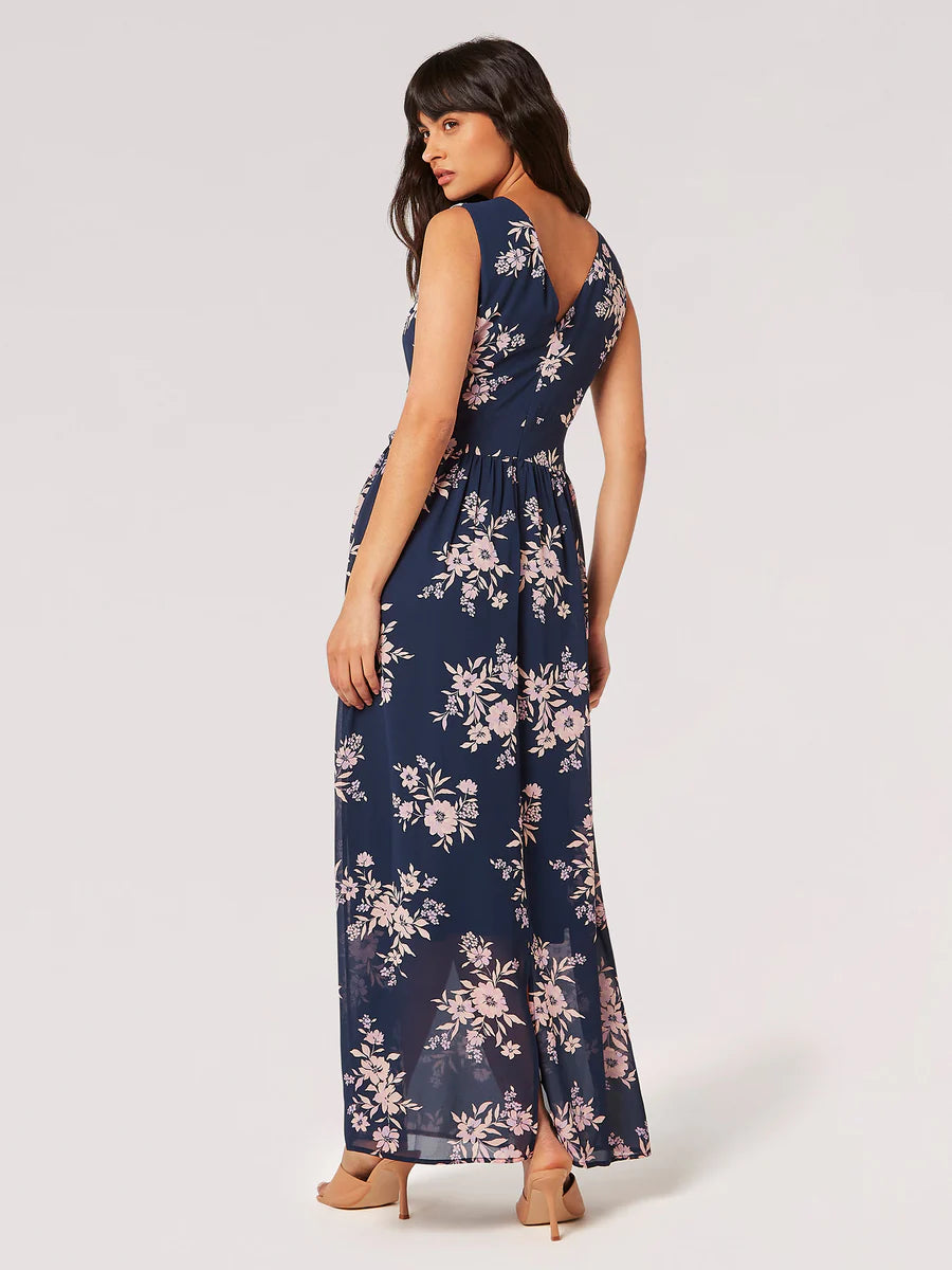 A woman posing in a sleeveless navy floral Apricot Blooms Maxi Dress with a belted waist and open-toe heels, perfect for her summer wardrobe.