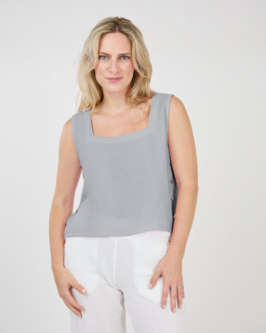Woman in a lightweight, Shannon Passero Elliana Sleeveless Side Button Top in gray and white pants standing against a light background.