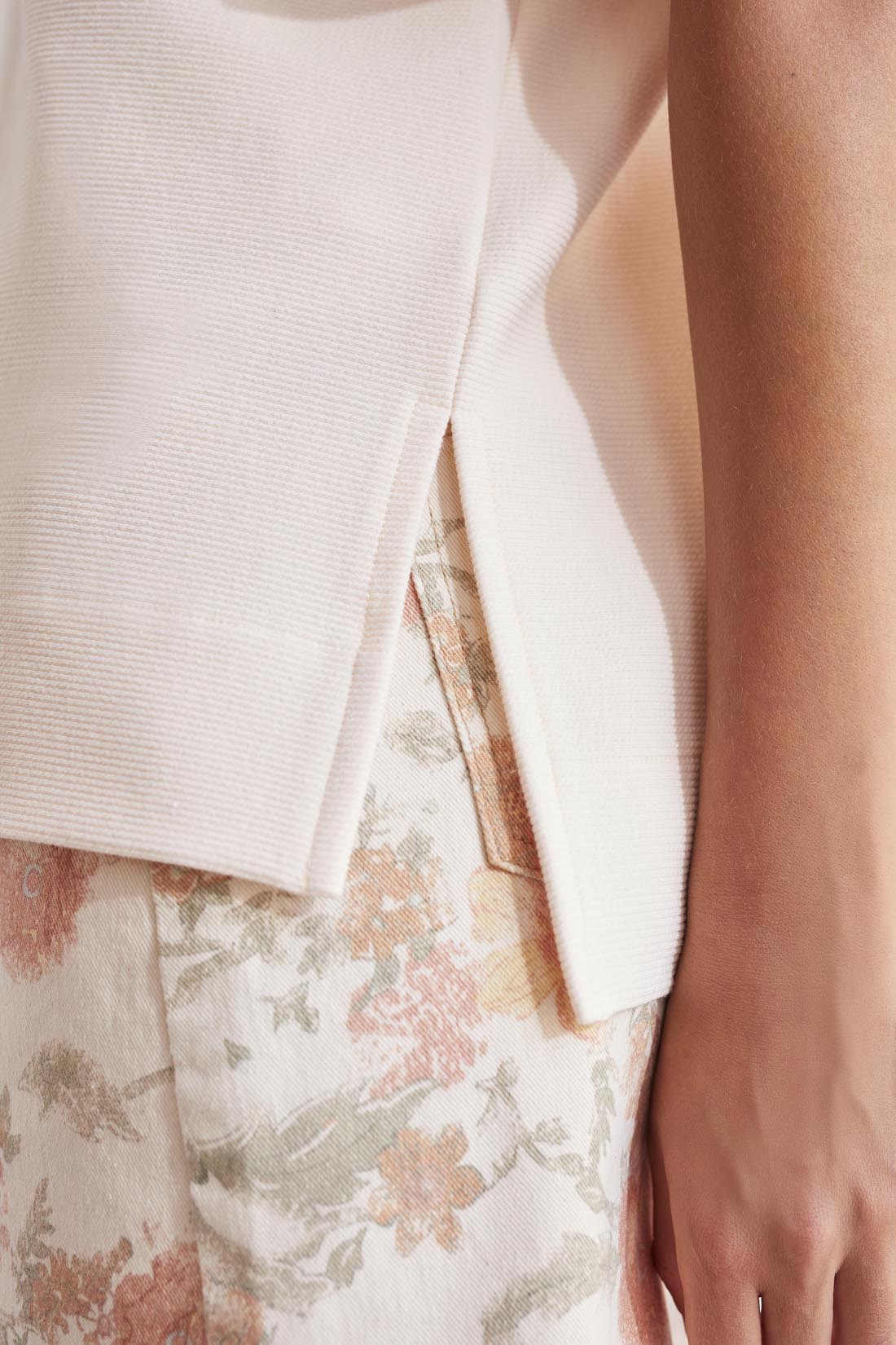 A close up of a woman wearing a white blouse with Tribal Elbow Sleeve Boat Neck With Side Slits and floral print pants.