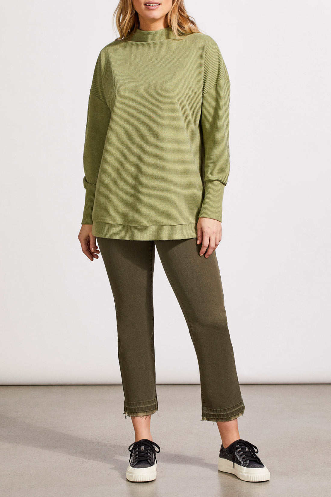 A person wearing a light green, long-sleeved knit sweater and green pants stands against a plain white background. The comfortable outfit includes the Funnel Neck Tunic by Tribal, which adds an extra touch of style.