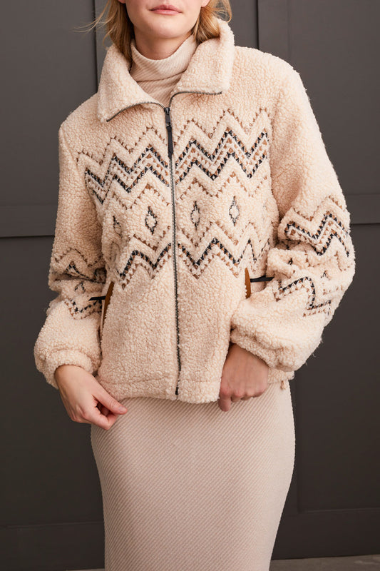 A person wearing a Tribal Lined Zip up Jacket with Embroidery in beige, paired with a matching ribbed dress, standing against a dark background.