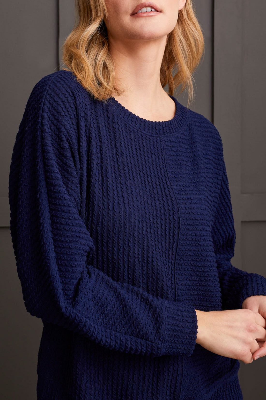 A person wearing a Tribal Crew Neck Dolman Sleeve Top in textured navy blue is shown from the shoulders to the waist against a dark background, showcasing ultimate comfort and style.