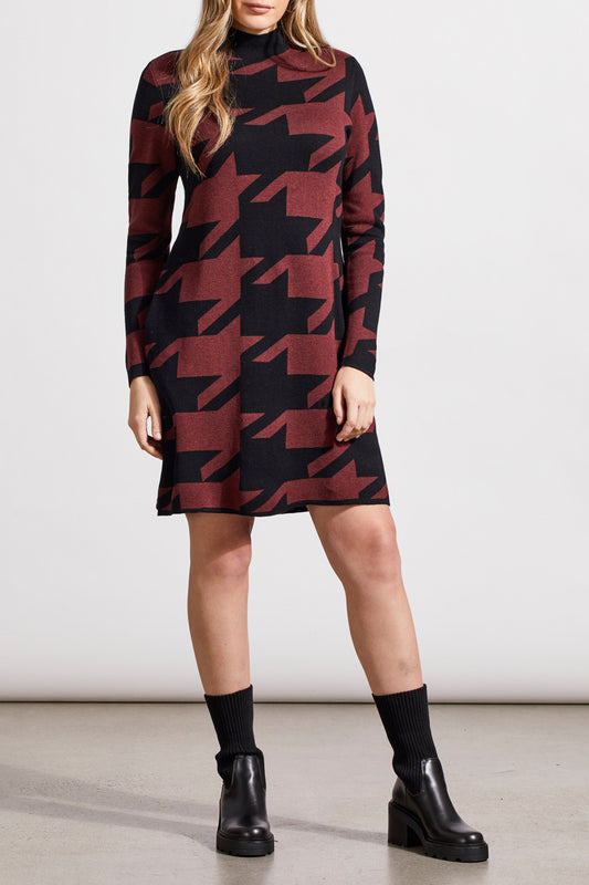 A person wearing a long-sleeved Tribal Funnel Neck Jacquard Sweater Dress in a red and black houndstooth pattern, paired with black ankle boots and black socks.