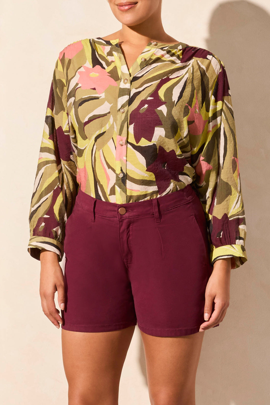 Against a plain backdrop, someone models a stylish long-sleeve blouse paired with Tribal's burgundy Pleated Wide Short featuring back elastic and pockets, effortlessly blending fashion and comfort.