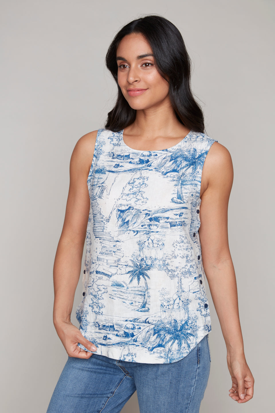 Donning the Carre Noir Palm Print Sleeveless Top, featuring a striking blue and white design, this individual pairs it effortlessly with blue jeans, exuding confidence against a plain backdrop.