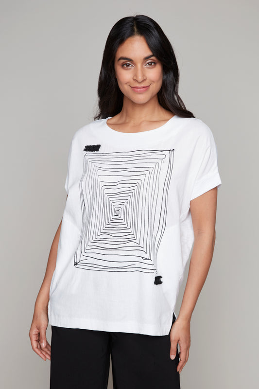 A person is wearing Carre Noir's Abstract Woven Top in white, with an abstract square pattern. They pair it with black pants and stand against a neutral background.