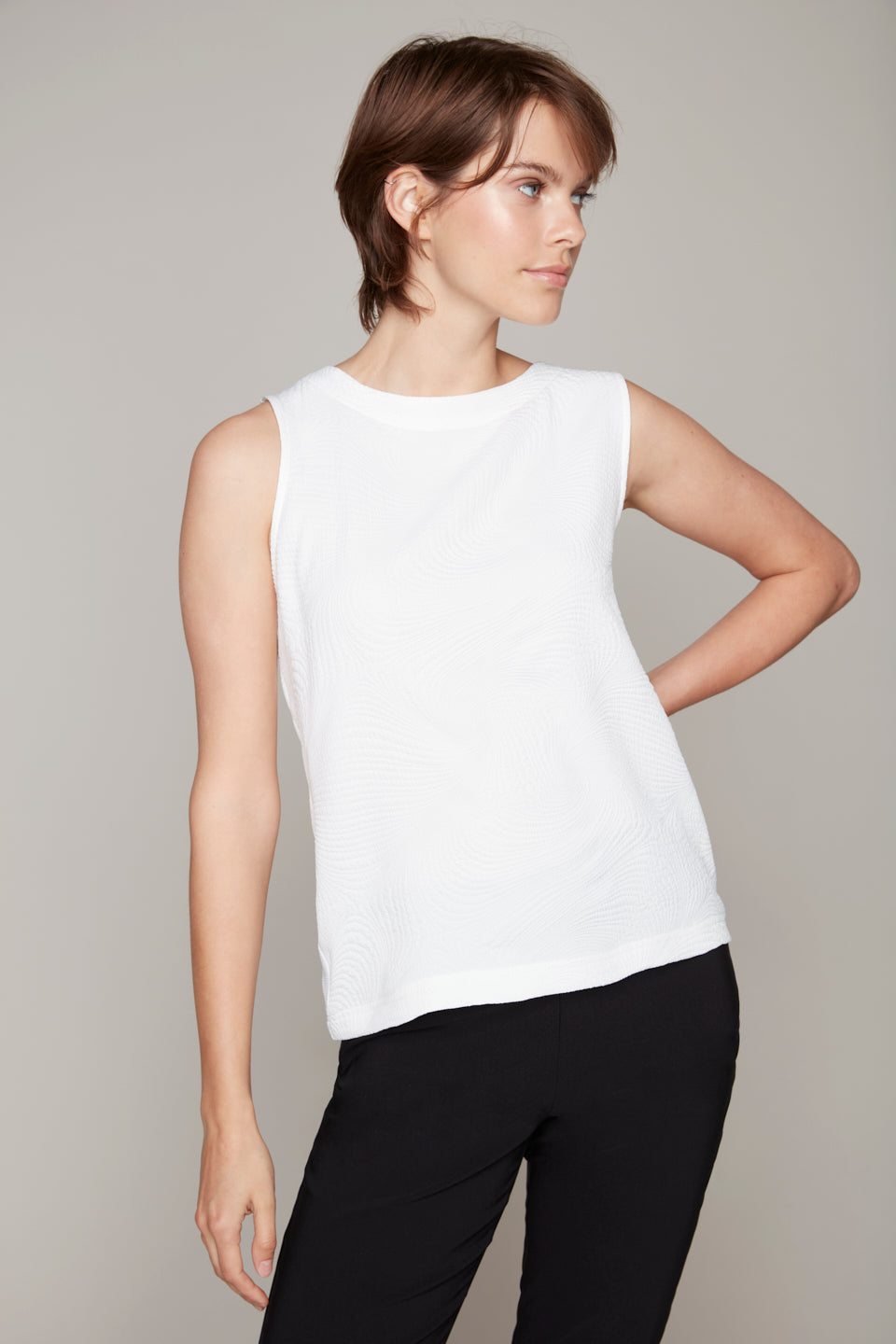 Against a plain backdrop, a person wears Carre Noir's Round Neck Sleeveless Top with blue jeans. The stylish back zip adds modern flair, and its lightweight fabric ensures comfort.