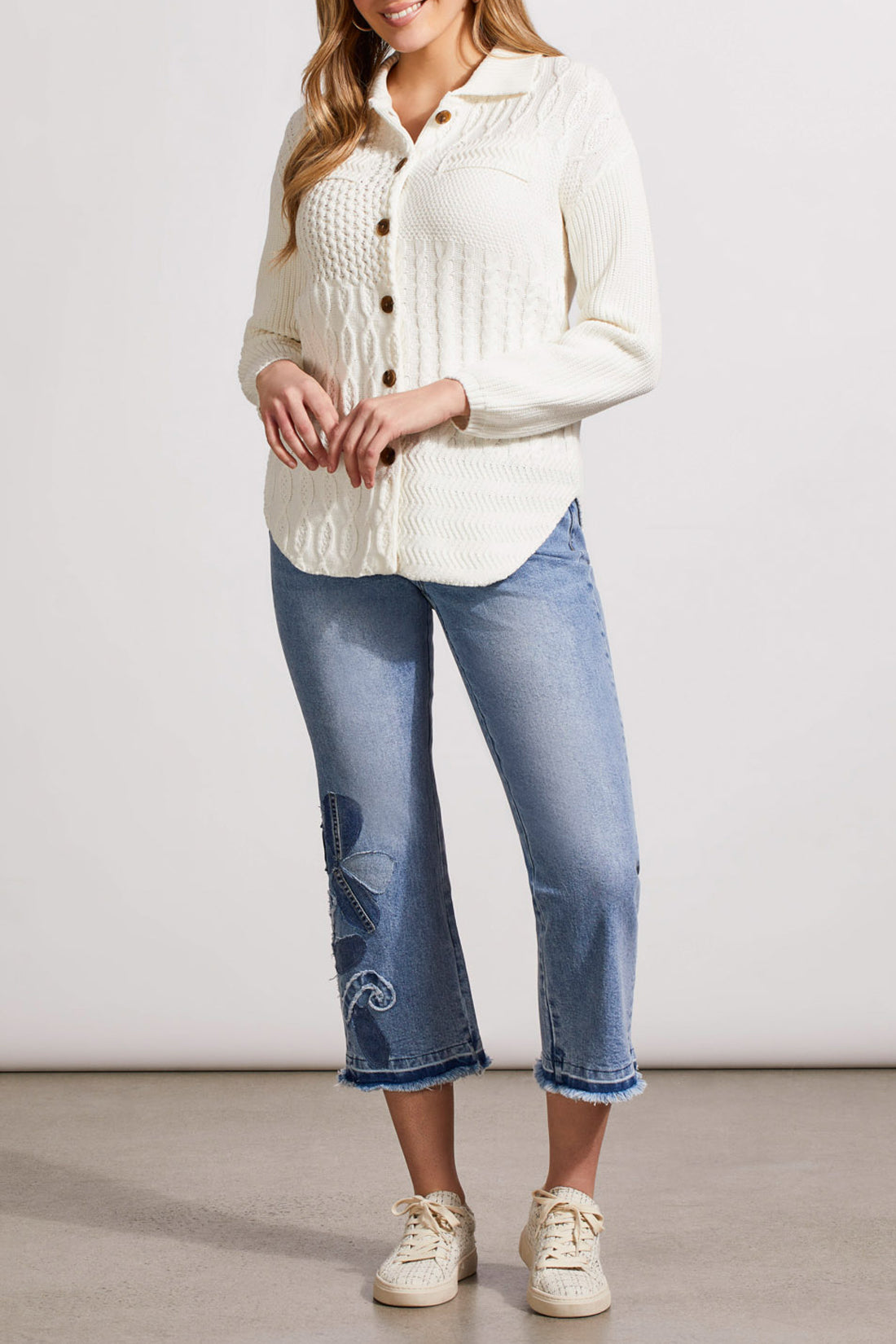 A person is wearing a stylish, white textured knit cardigan from Tribal, known as the Sweater Shacket with Wash Effect, adorned with wooden buttons. The person is holding the collar of the shacket with their left hand.