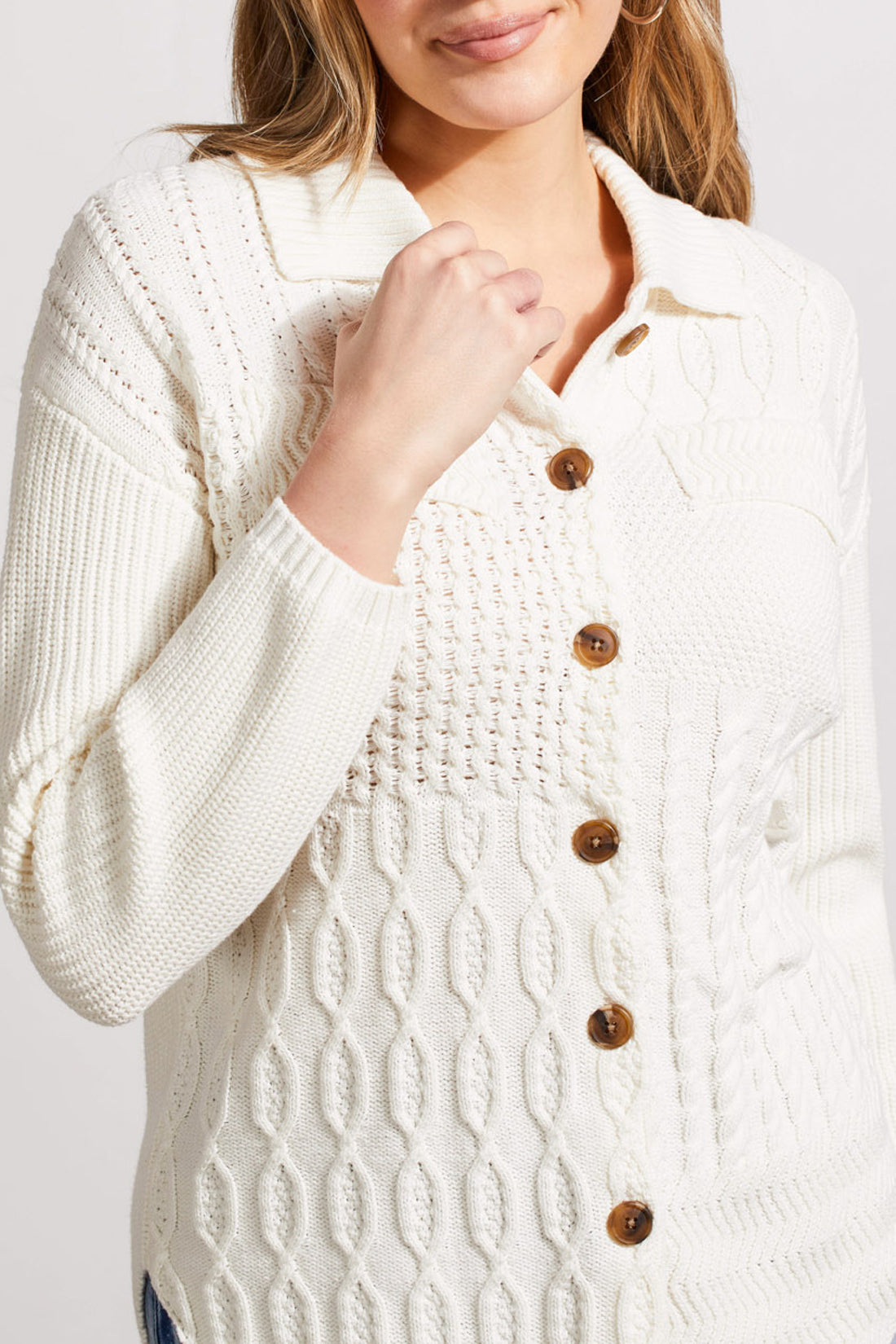 A person is wearing a stylish, white textured knit cardigan from Tribal, known as the Sweater Shacket with Wash Effect, adorned with wooden buttons. The person is holding the collar of the shacket with their left hand.