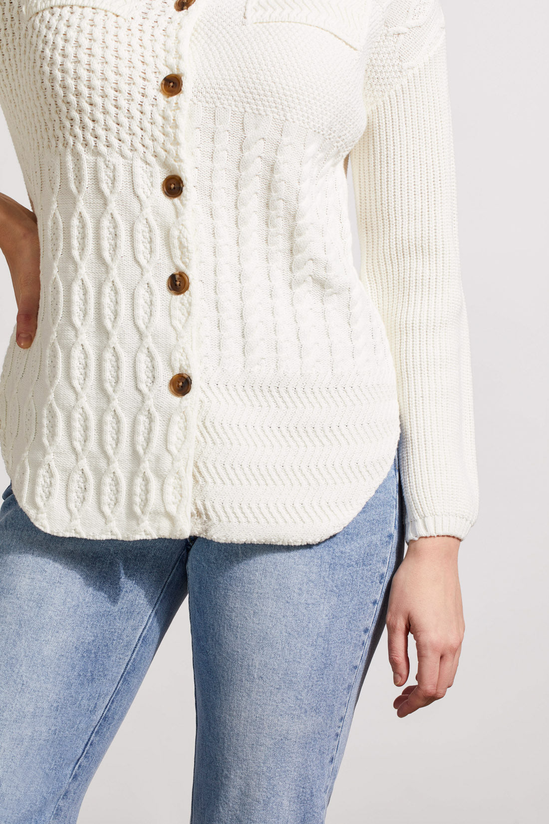 A person is wearing a stylish, white textured knit cardigan from Tribal, known as the Sweater Shacket with Wash Effect, adorned with wooden buttons. The person is holding the collar of the shacket with their left hand.