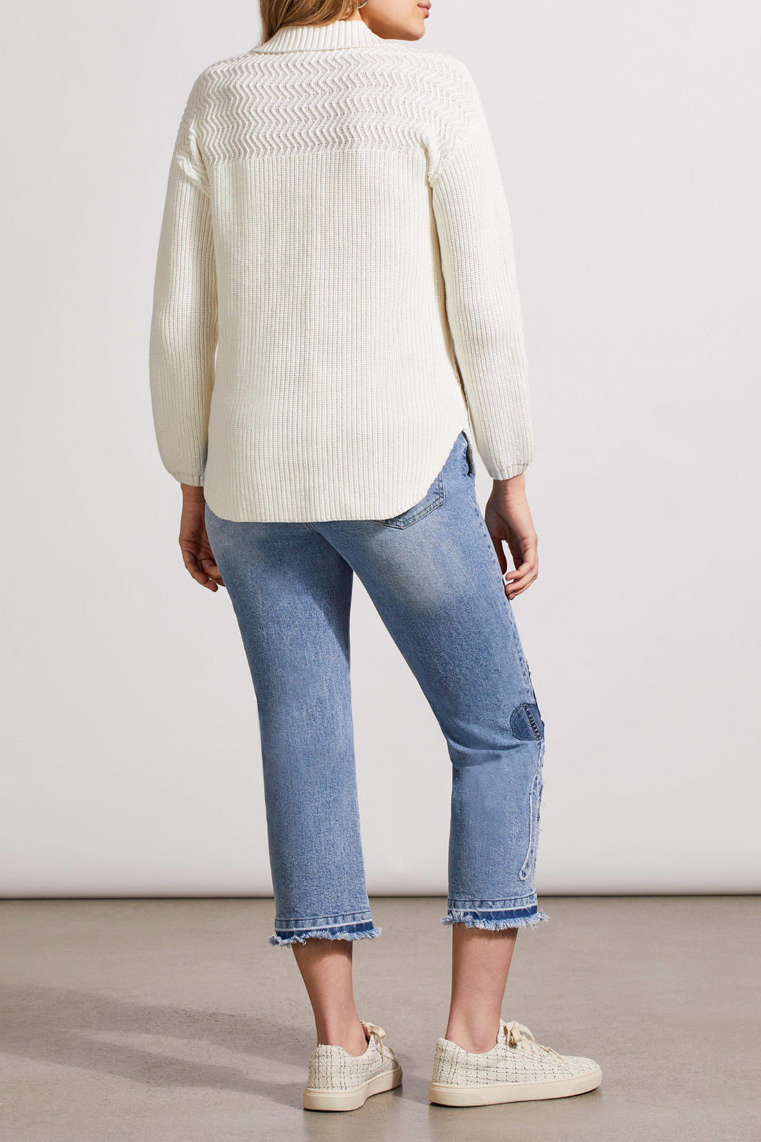 A person is wearing a stylish, white textured knit cardigan from Tribal, known as the Sweater Shacket with Wash Effect, adorned with wooden buttons. The person is holding the collar of the shacket with their left hand.