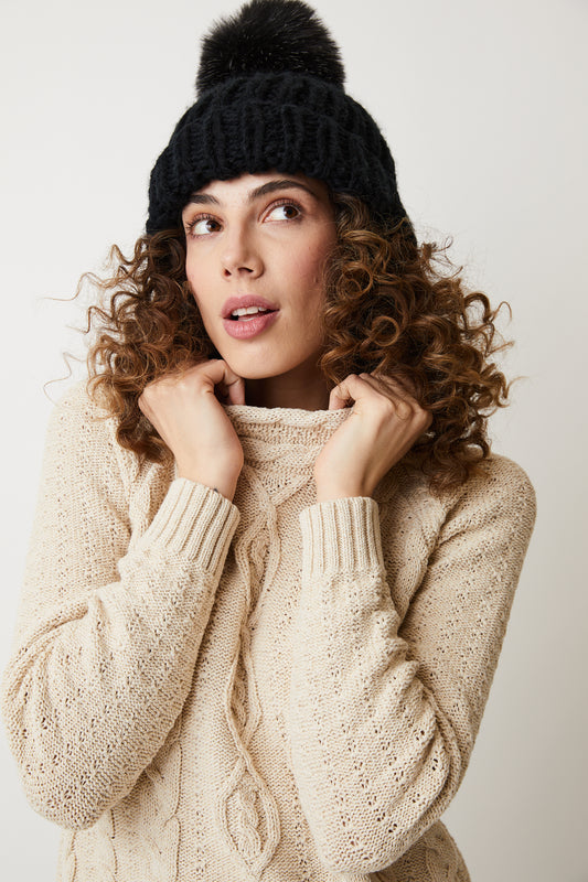 Parkhurst Samira Sweater- A woman wearing a cozy beige sweater and a pom pom hat.