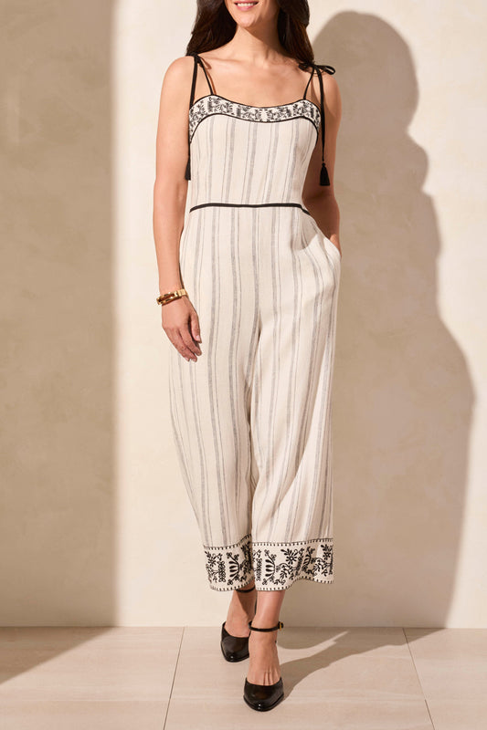 A person wearing the Tribal Sleeveless Jumper with Pockets—white and black striped with detailed borders and tassels, paired with black heels and a bracelet.