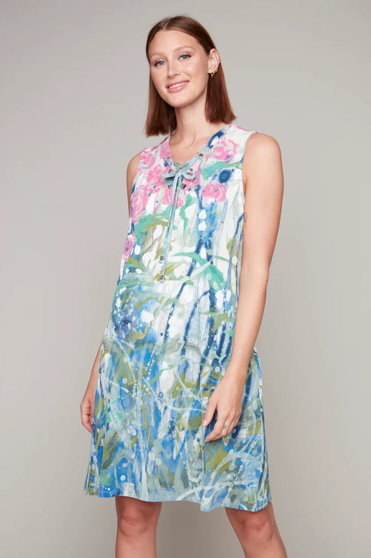 A woman in a Claire Desjardins sleeveless dress with lace-up detail, featuring a colorful floral pattern, stands against a plain background.