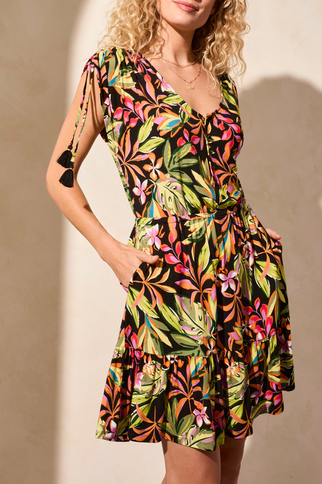 A person in Tribal's Adjustable Cap Sleeves V-Neck Dress-Melon, featuring a green, pink, and yellow floral pattern, stands on a light floor. The charming adjustable cap sleeves are elegantly paired with brown strappy heels.