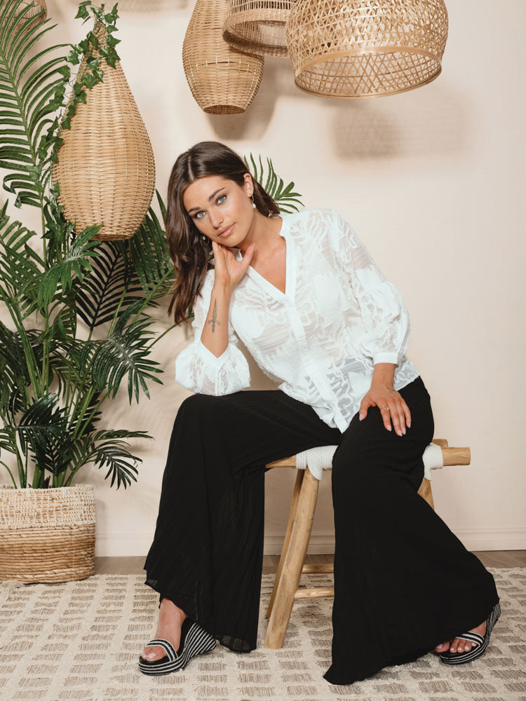 A fashion-forward woman wearing a white blouse and Alison Sheri's Pleated Super Wide Leg Pants with a folded design.