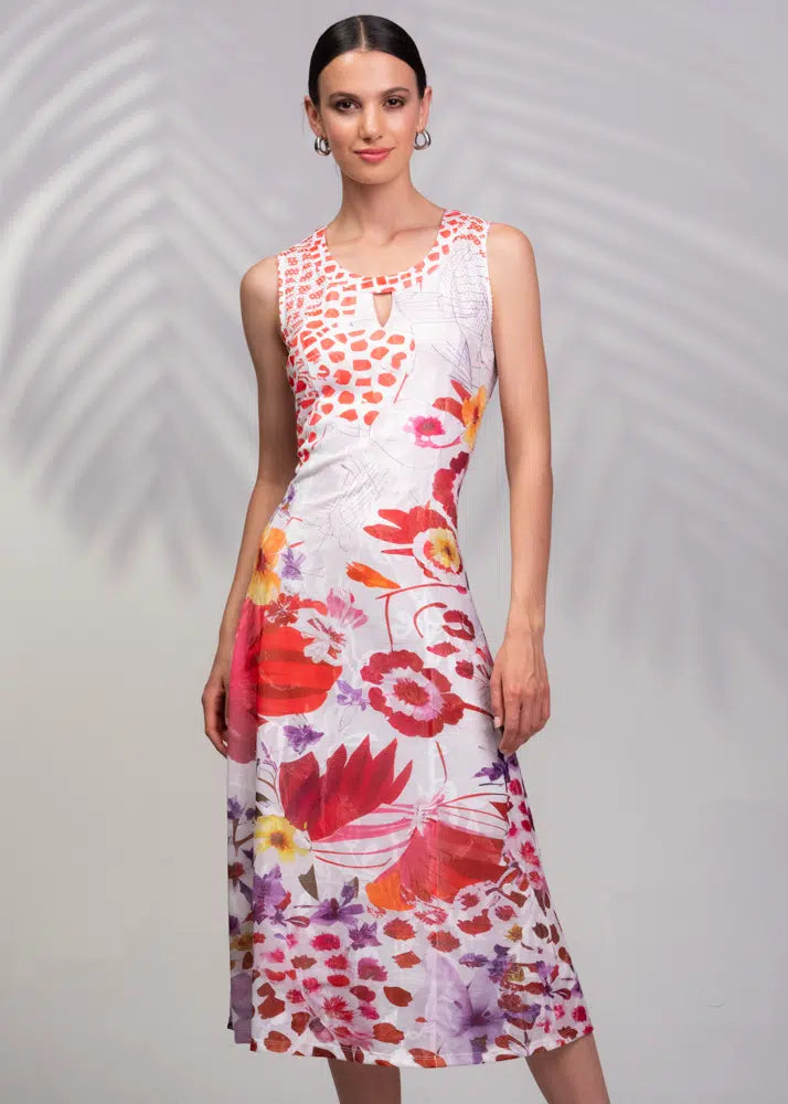 A woman stands gracefully in a sleeveless Key Hole Flower Dress by Alison Sheri, showcasing floral prints with red, pink, and purple accents against a gray background featuring a subtle leaf pattern.