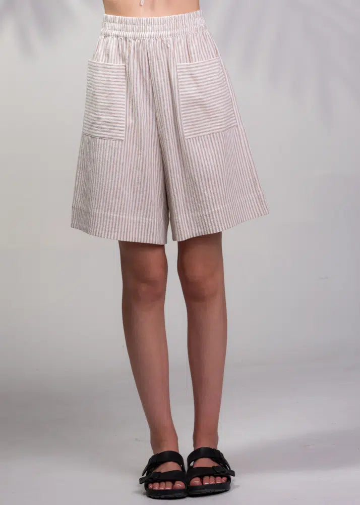 An individual is modeling a pair of Alison Sheri Striped Shorts with large front pockets, paired with black sandals, against a plain background.