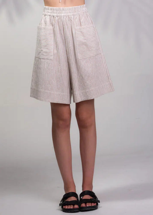 An individual is modeling a pair of Alison Sheri Striped Shorts with large front pockets, paired with black sandals, against a plain background.