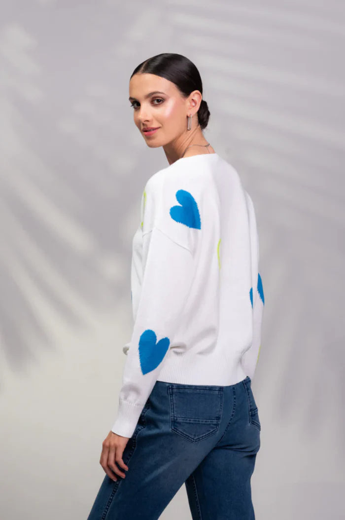 Someone wearing a chic Blue Heart Sweater by Alison Sheri, featuring long sleeves with blue and yellow heart patterns, paired with blue jeans.