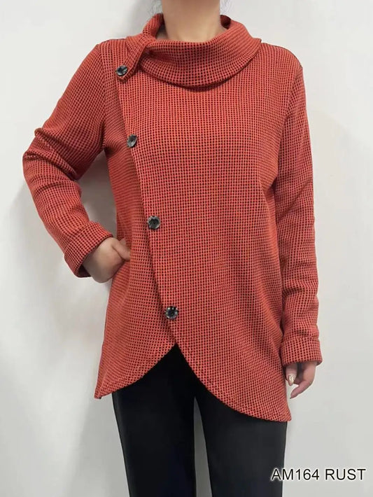 A person wearing the Winnie Top by Creation, a long-sleeve button-up with a high collar in rust color, pairs it with black pants and stands against a plain background.