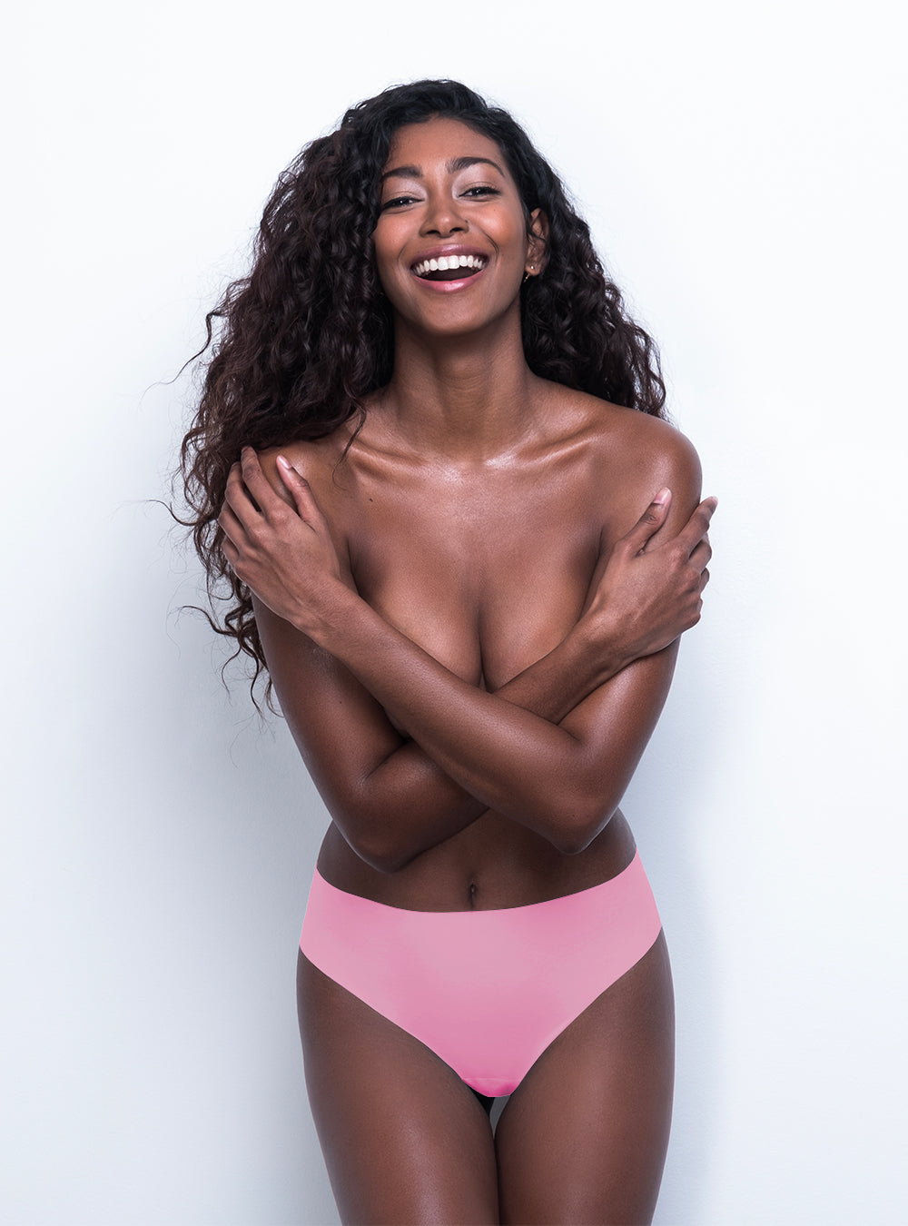 A smiling woman with curly hair covering her chest with her arms, wearing comfortable floral Body Hush 365 Bikini bottoms against a white background.